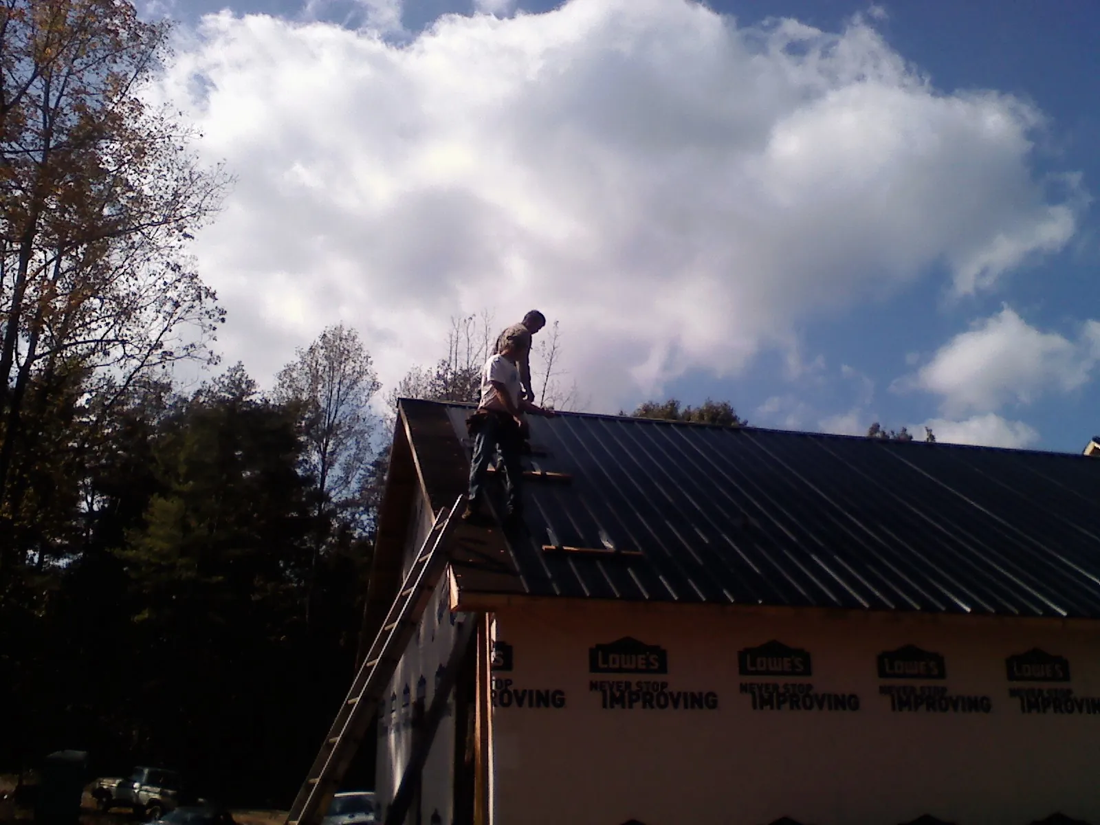 Roofer fastening dark metal panels high against a cloudy sky, from a Roof Inspection job in Belmont