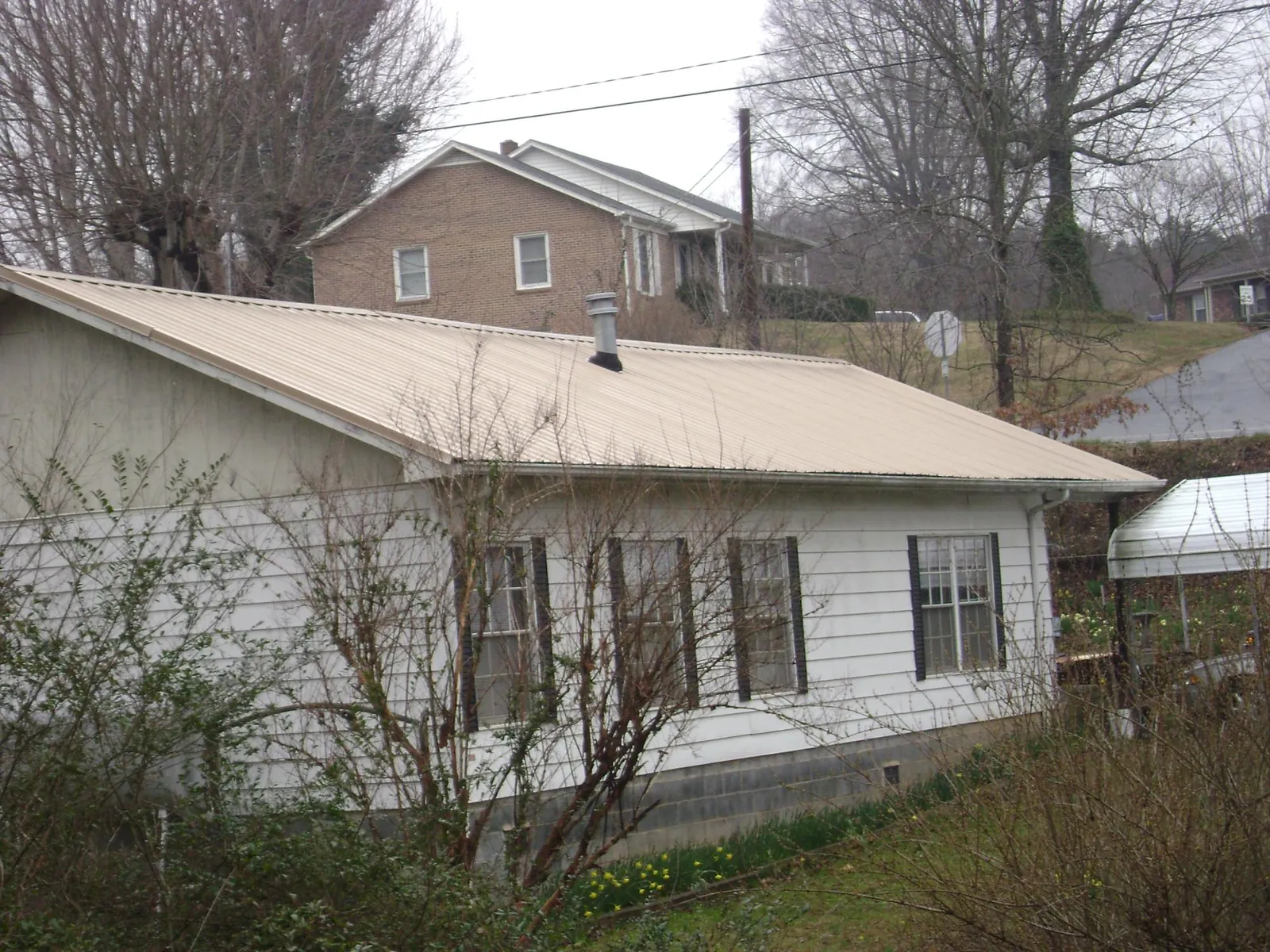 Tan metal roof on a white sided house set into a hillside — Commercial Roofing by Roofing Brothers in Belmont